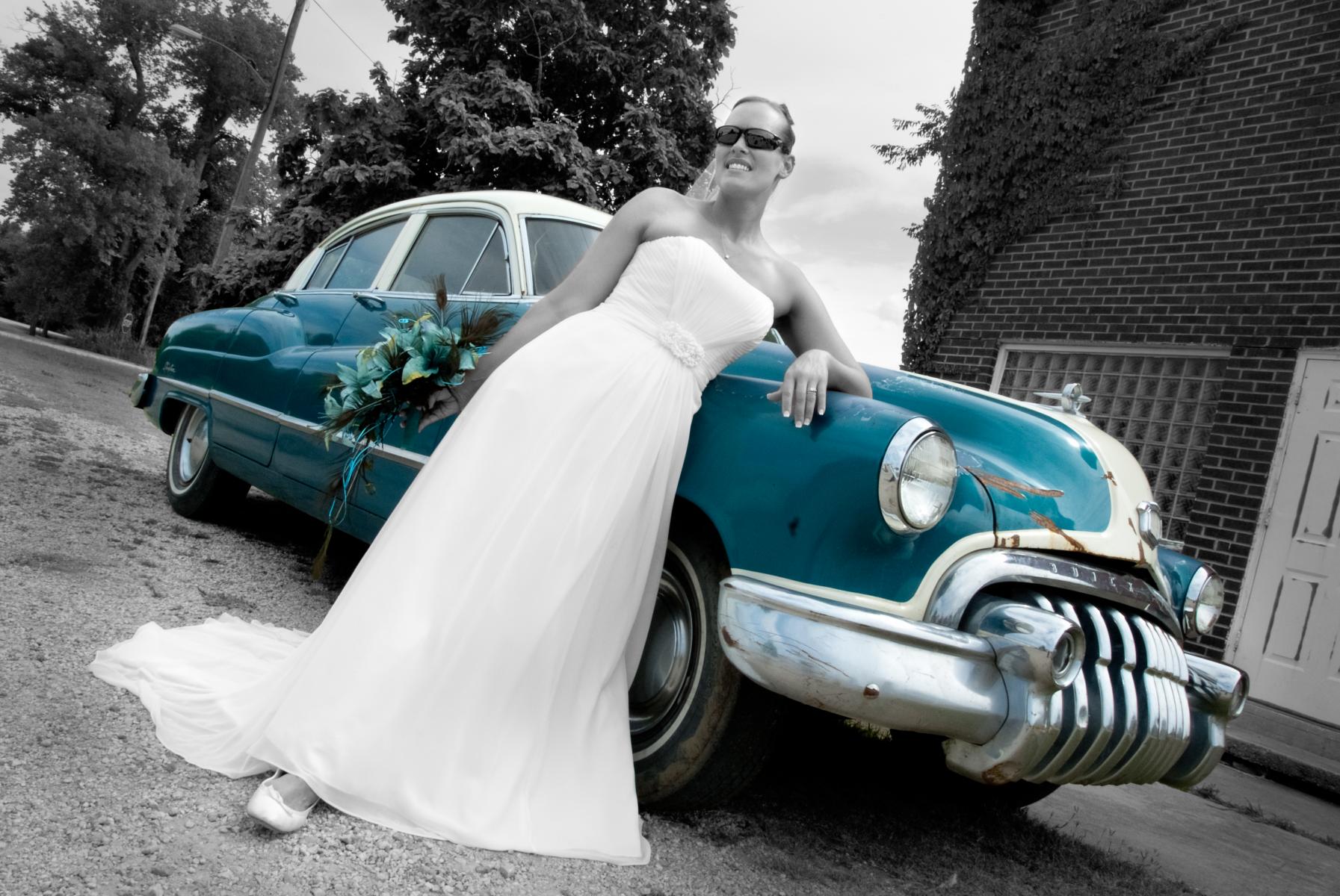 Wedding dress is accentuated against a classic car by the low angle of the camera in this selective color bridal photo, by Robertsons' Warehouse Photography, Wichita, KS